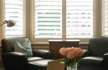 how-window-shutters-can-help-reduce-your-energy-bills A modern office space with two leather chairs, a laptop on a desk, and stylish interior shutters for natural light control.